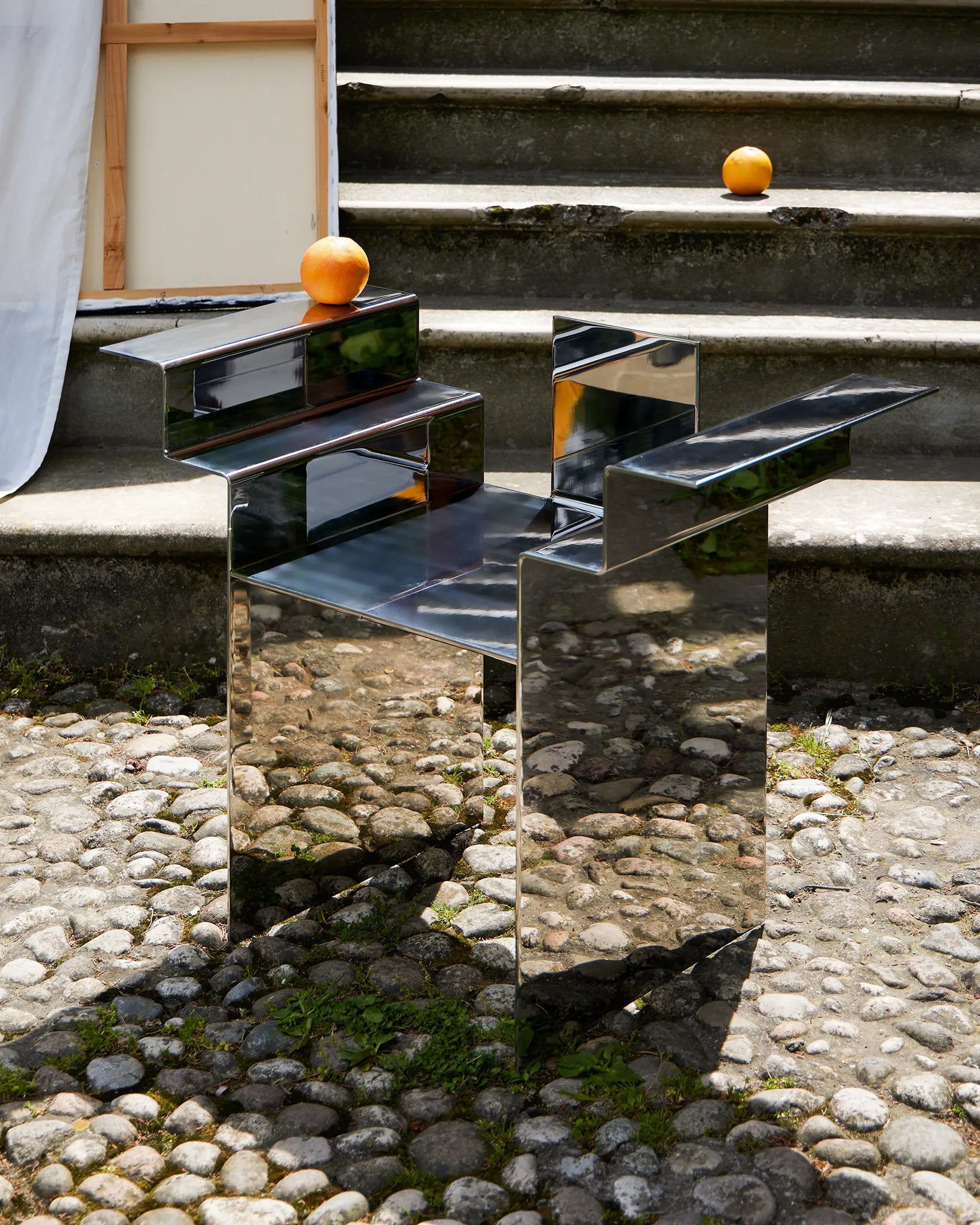 detail of a stainless-steel mirror chair with mesoamerican temple-like shape, with scene props like an orange and a curtain