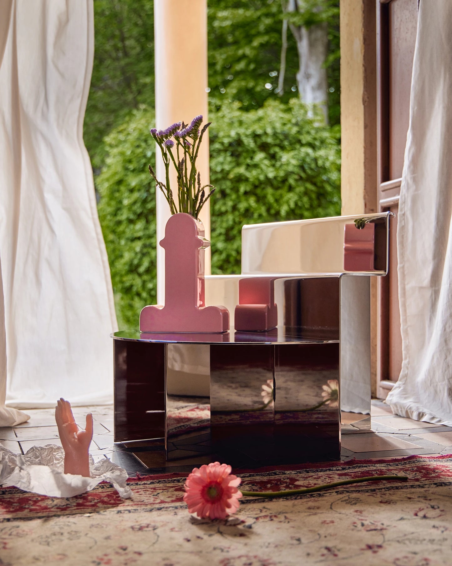 stainless-steel mirror chair with mesoamerican temple-like shape, in a domestic environment with white curtains, pink props and persian carpet