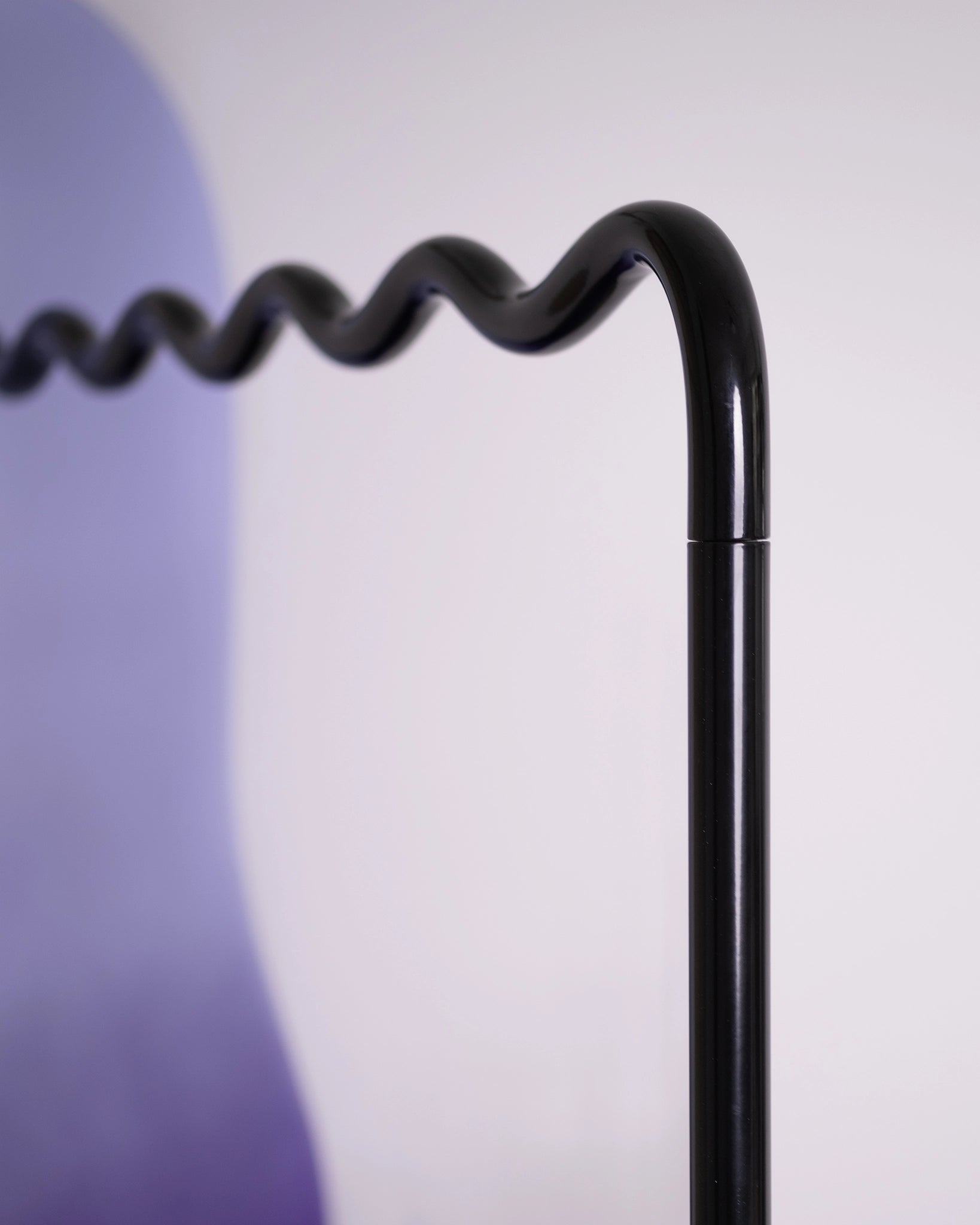 detail of a clothing rack with soft shapes and a wavy metal hanging tube, purple gradient